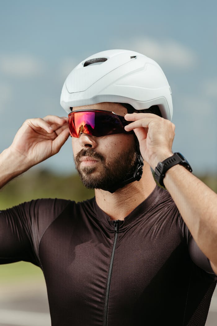 Male cyclist adjusts sunglasses while wearing a white helmet outdoors.
