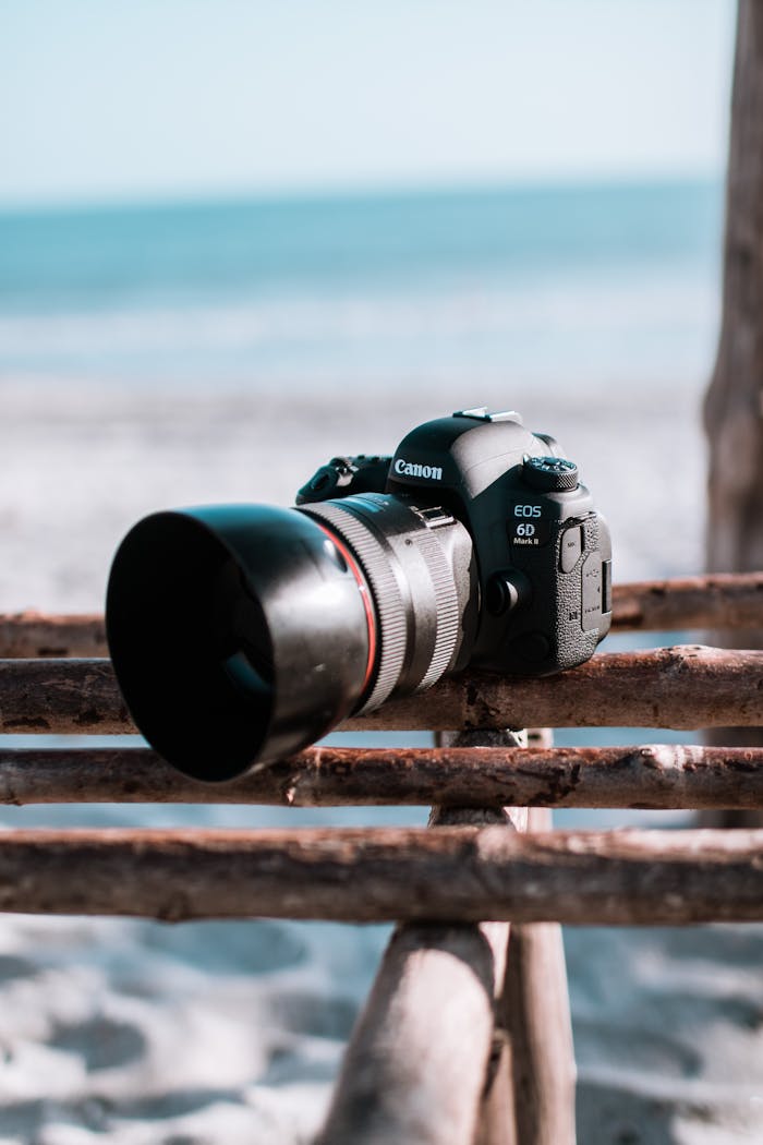 Canon DSLR camera placed on wooden fence at a serene beach setting.